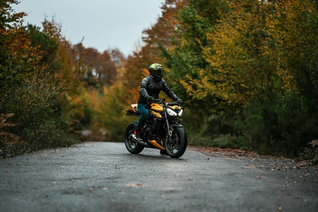 A motorcyclist in protective gear rides through a scenic autumn forest path.
